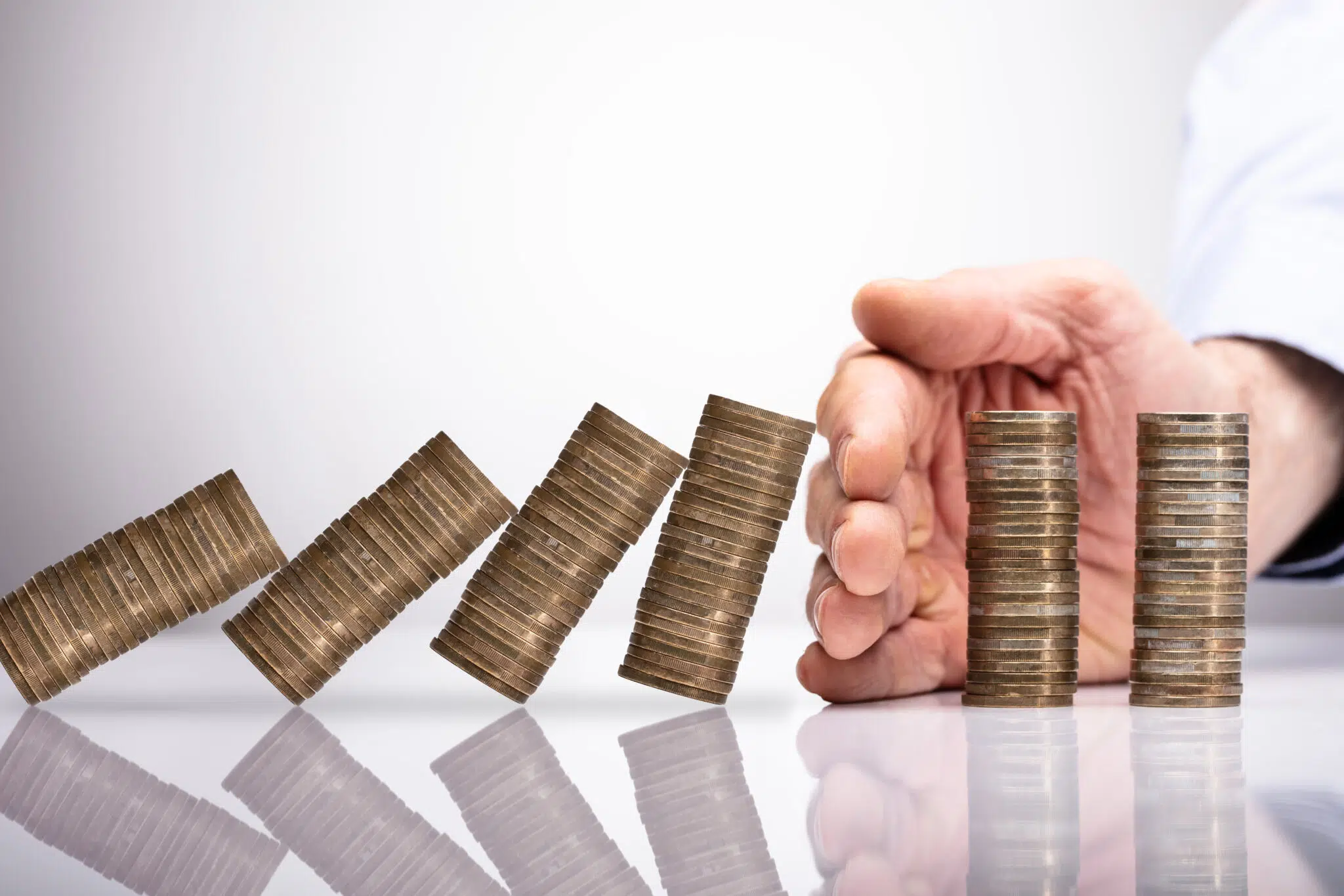 Close-up Of A Businessperson's Hand Protecting Stacked Coins From Falling On Reflective Desk