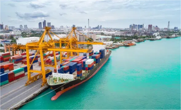 An image of a ship docked at a shipyard with several shipping containers