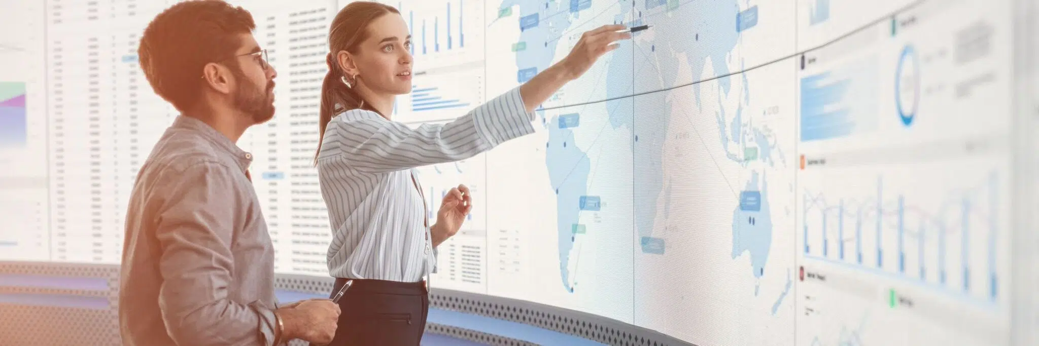 man and woman looking at screen with global map and graphs